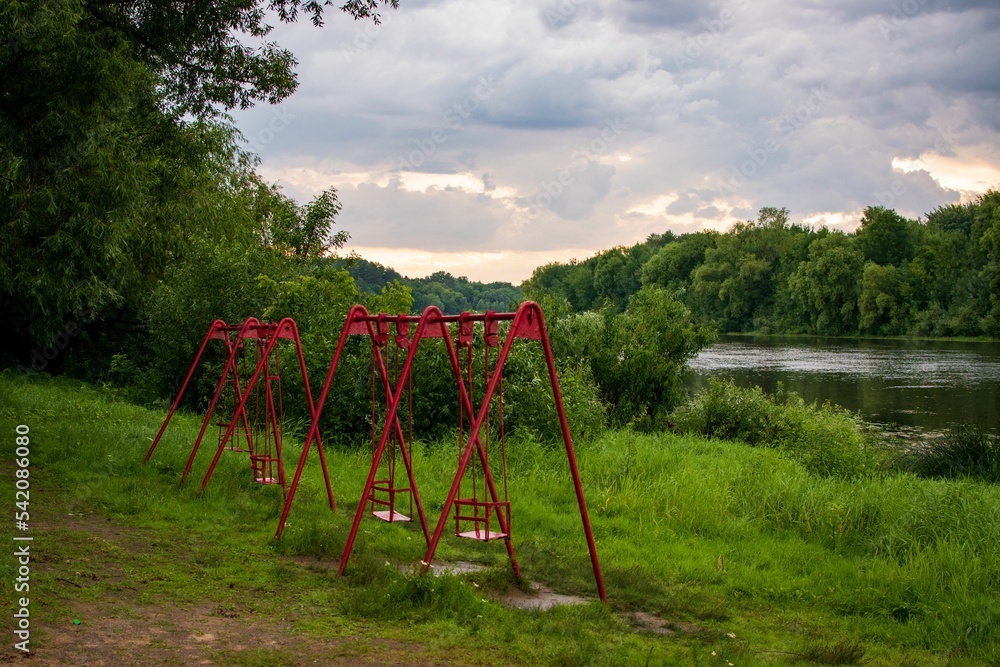 Swings on the river bank surrounded by vegetation and grass Swings on the river bank surrounded by vegetation and grass