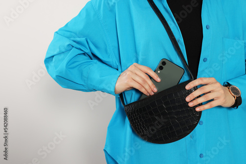 Woman putting smartphone into stylish bag on white background, closeup. Space for text photo