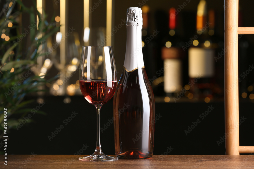 Bottle and glass of delicious rose wine on wooden table in bar
