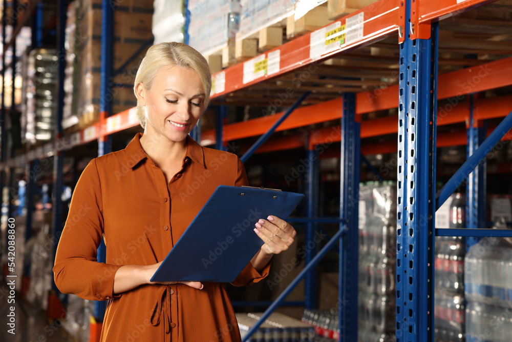 Happy manager holding clipboard in warehouse with lots of products