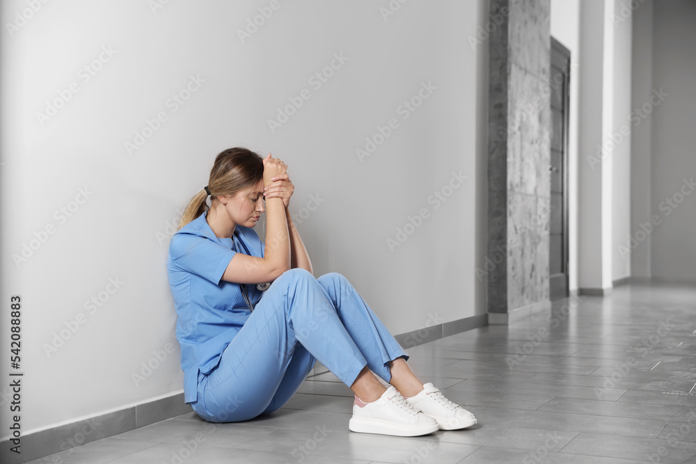 Exhausted doctor sitting on floor in hospital, space for text