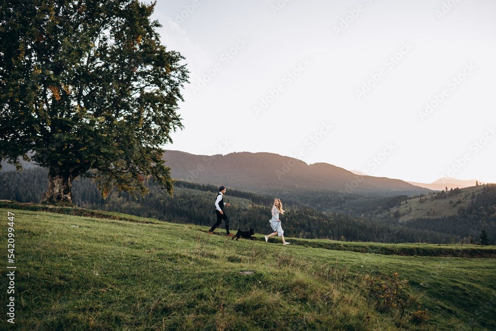 Funny beloved couple running down hill with dog. Funny beloved couple running down hill with dog.