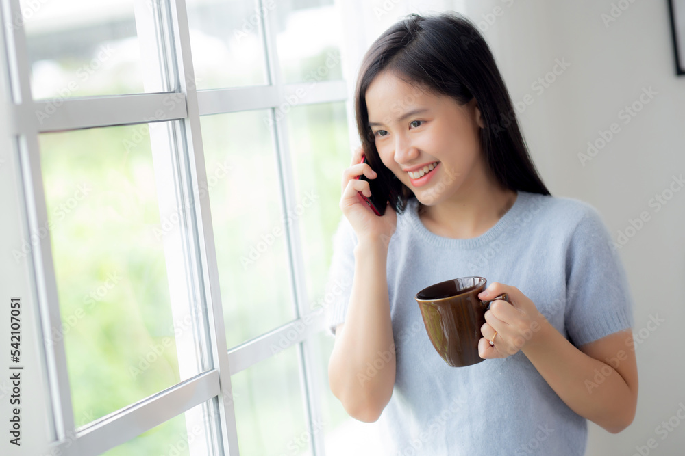 Happiness young asian woman talking with smartphone in the living room at home, female speaking with smart phone and hold coffee cup while relax and cozy at home, lifestyles and communication concept. Happiness young asian woman talking with smartphone in the living room at home, female speaking with smart phone and hold coffee cup while relax and cozy at home, lifestyles and communication concept.