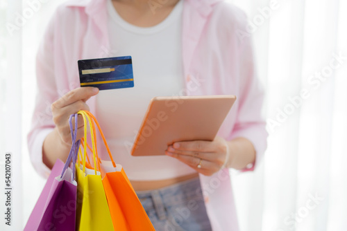 Hands of young asian woman standing using digital tablet shopping online with credit card while holding paper bag, female paying with transaction financial, purchase and payment, business concept.