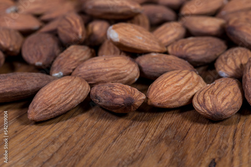 Whole almonds, scattered on a wooden board. Almond fruit seeds. Edible raw, and suitable for preserves. Almonds are a valuable source of micro and macro elements and monounsaturated fatty acids.