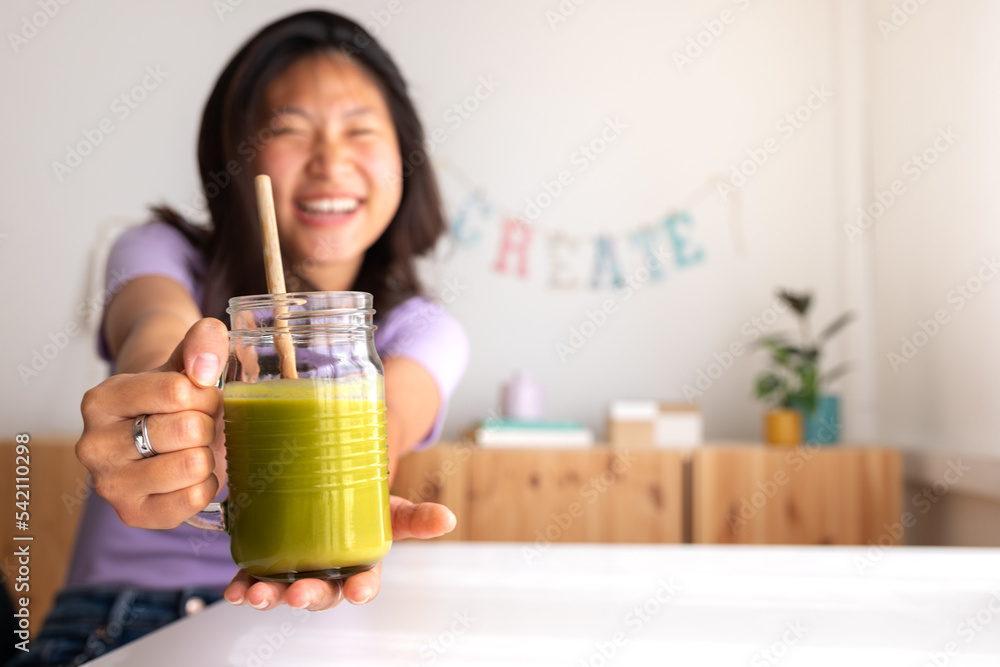 Happy teen asian female student showing healthy green juice at camera. Focus on juice. Copy space. Healthy lifestyle Happy teen asian female student showing healthy green juice at camera. Focus on juice. Copy space. Healthy lifestyle