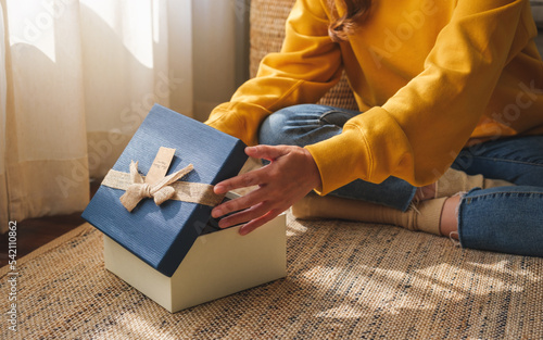 Closeup image of a young woman receiving and opening a gift box at home