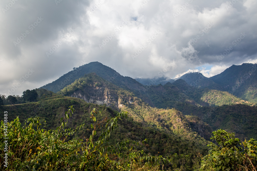 Rainclouds brush lush forest mountains with sunshine near Lake Atitlan, Guatemala.