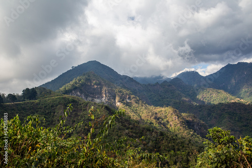 Rainclouds brush lush forest mountains with sunshine near Lake Atitlan, Guatemala.