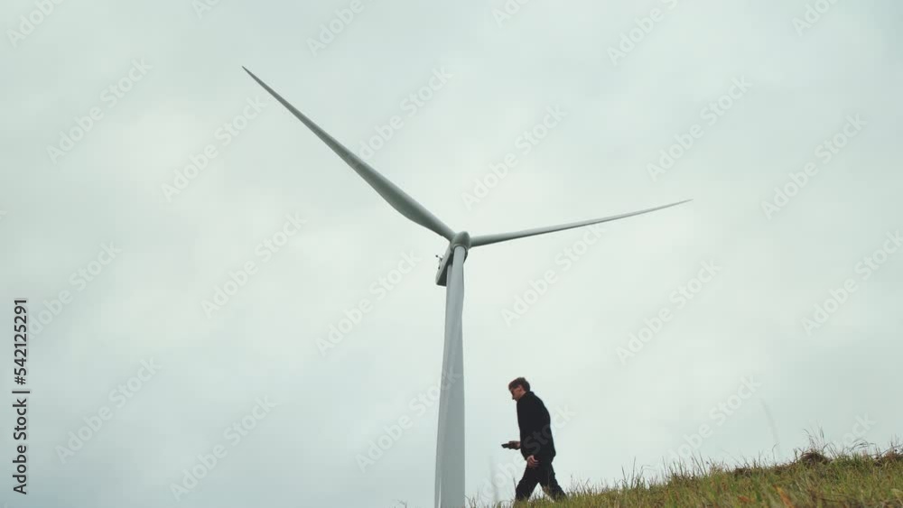 Stylish man and wind turbine, symbol of renewable energy, windmill, cloudy sky Stylish man and wind turbine, symbol of renewable energy, windmill, cloudy sky