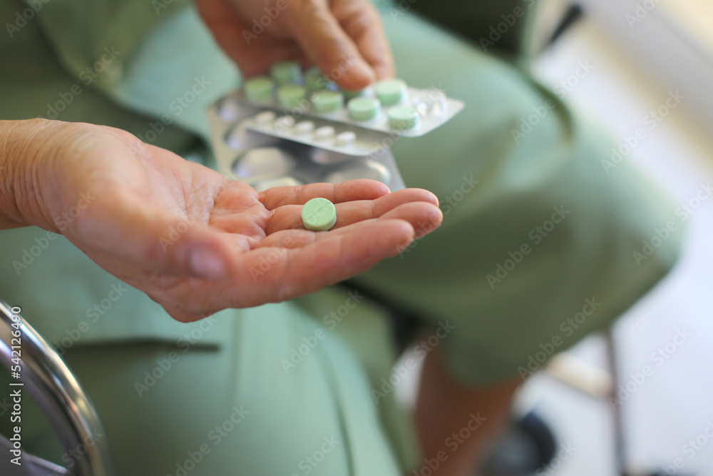 Closeup on Medicine Pills on hand of patient sitting on wheelchair.