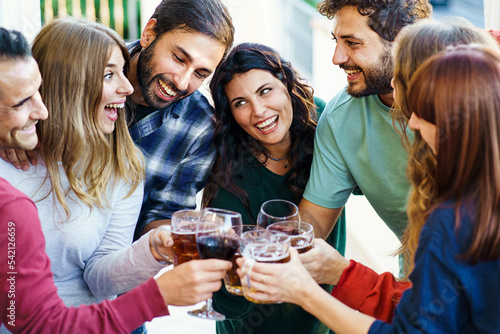 Group of happy friends cheering together toasting beer and wine standing on the balcony -