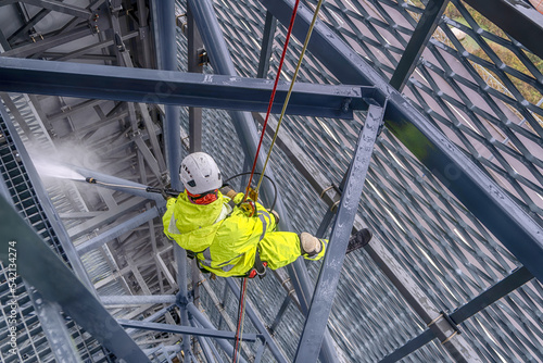 Rope access technicians clean the structure with a high-pressure cleaner