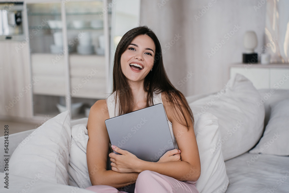 Excited Attractive asian woman screaming smiling happy, received gift, new laptop, sitting on couch with big cushions at home. Gorgeous Korean businesswoman hugs laptop against blurry living room.