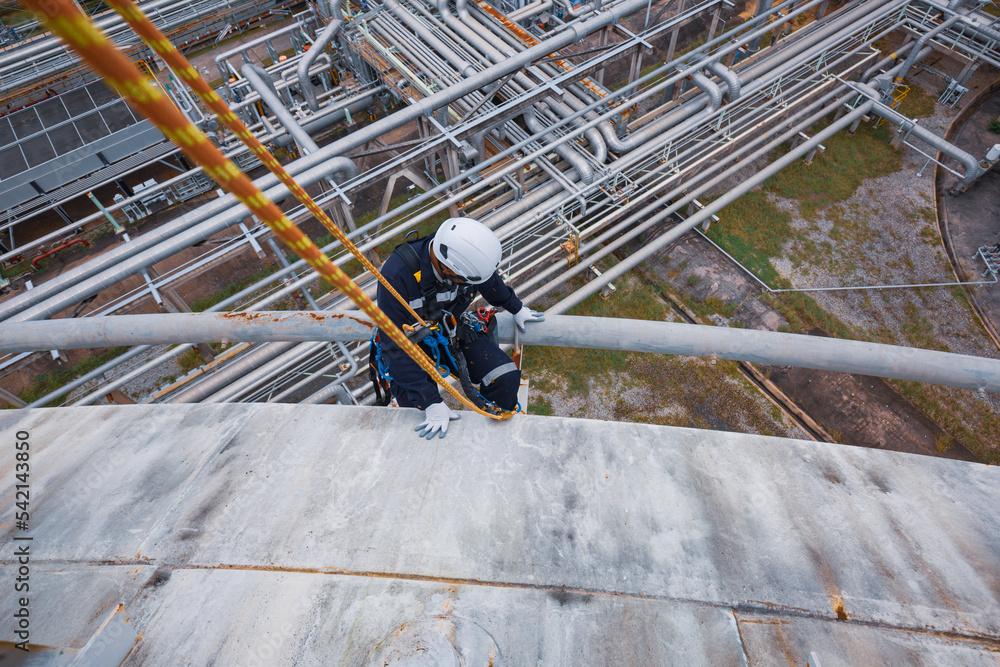 Male worker inspection wearing safety first harness rope safety line working at a high place underside steel long pipes insulation flowing and pipe elbow