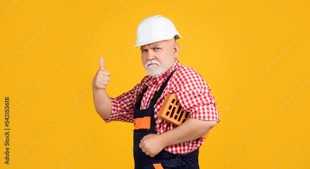 serious old aged man bricklayer in helmet on yellow background serious old aged man bricklayer in helmet on yellow background