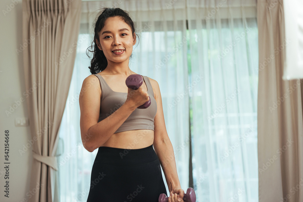 Asian woman exercise at home. Young healthy female in sportswear workout training with dumbbell in living room, Health care and wellness concept.