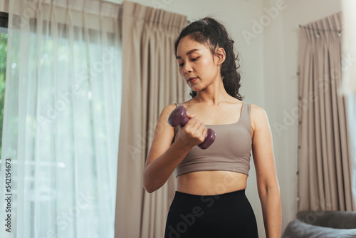 Asian woman exercise at home. Young healthy female in sportswear workout training with dumbbell in living room, Health care and wellness concept.