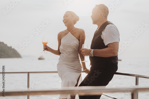 Romantic couple love having cocktails on yacht. Happy man and woman standing and drinking wine in cruise ship while sunset on vacation. luxury and honeymoon lifestyle.