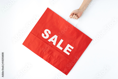 Hand holding red craft shopping bag with sign SALE. Minimal Black Friday shopping, sale, promotion advertising concept