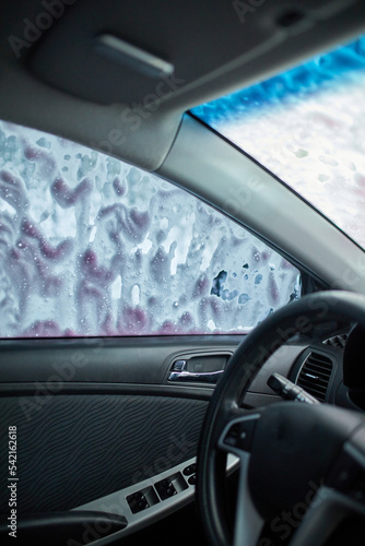 Man washing his car, using pink active foam on self service washing, contactless high pressure water jet.