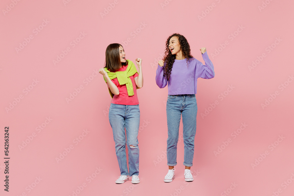 Full size young two friend overjoyed happy fun cool cheerful smiling women 20s wear green purple shirts together do winner gesture isolated on pastel plain light pink color background studio portrait