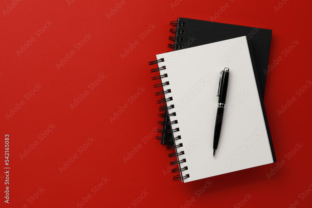Notebooks and pen on red background, top view. Space for text Notebooks and pen on red background, top view. Space for text