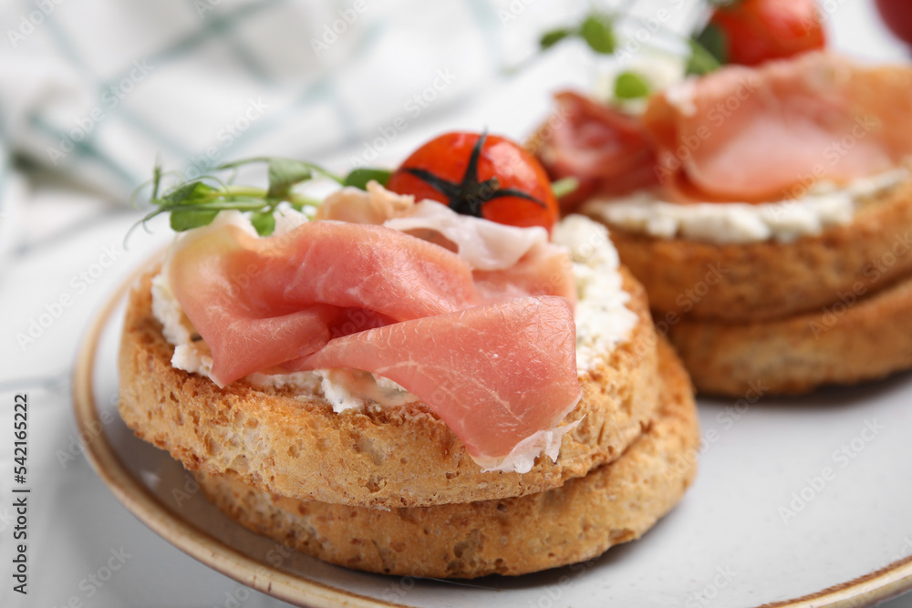 Tasty rusks with prosciutto, cream cheese and tomatoes served on white table, closeup Tasty rusks with prosciutto, cream cheese and tomatoes served on white table, closeup