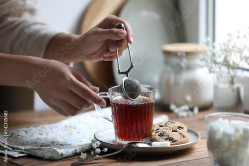 Young woman using snap infuser for brewing tea at wooden table, closeup photo