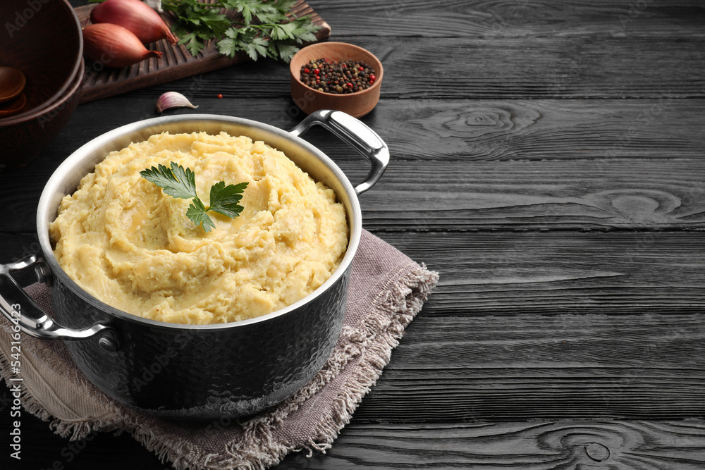 Pot of tasty mashed potatoes with parsley on black wooden table. Space for text Pot of tasty mashed potatoes with parsley on black wooden table. Space for text