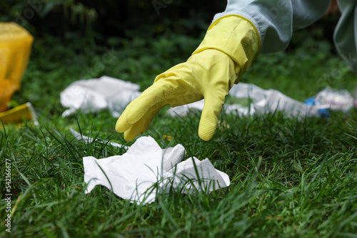 Woman collecting garbage on green grass, closeup