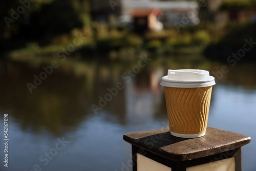 Takeaway paper cup with coffee near river outdoors. Space for text