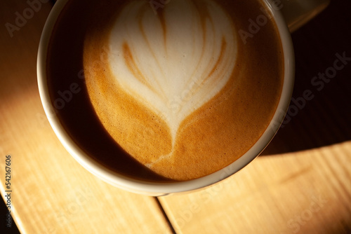 Cup of cappuccino on wooden table under morning light. Close up