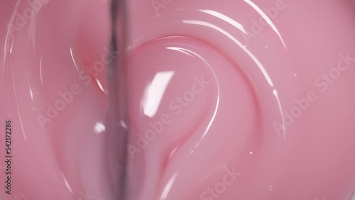 The spatula stirs the thick gel nail polish of light pink color, close-up