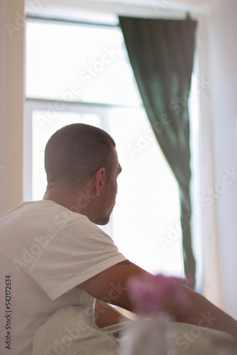 Man sitting on bed in early morning and looking forward. Back view of Caucasian man waking up from sound sleep, preparing for getting out of bed. Dream, sleeping concept