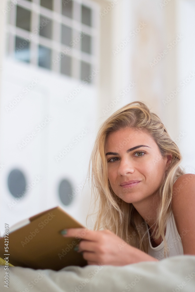 cPretty woman lying on bed, holding book and looking at camera, Vertical shot of beautiful and cheerful woman reading book in early morning, devoting time to hobby. Morning routine, education concept cPretty woman lying on bed, holding book and looking at camera, Vertical shot of beautiful and cheerful woman reading book in early morning, devoting time to hobby. Morning routine, education concept