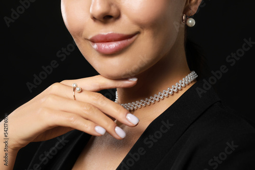 Young woman with elegant pearl jewelry on black background, closeup