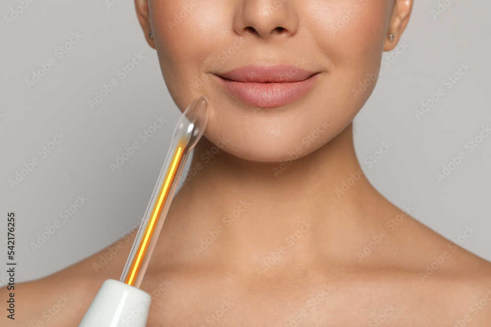 Woman using high frequency darsonval device on grey background, closeup