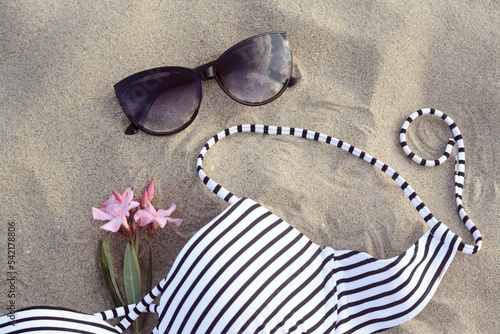 Beautiful sunglasses, swimsuit and tropical flower on sand