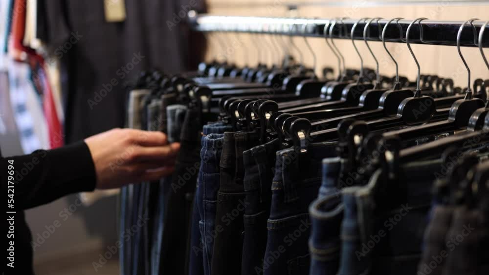 Rack with jeans in a clothing store. Different jeans on a hunger. Human hand goes over jeans