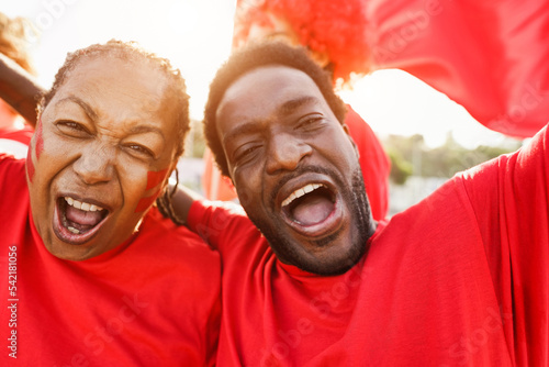 African red sport fans screaming while supporting their team - Football supporters having fun at competion event - Champions and winning concept - Focus on left senior woman eye