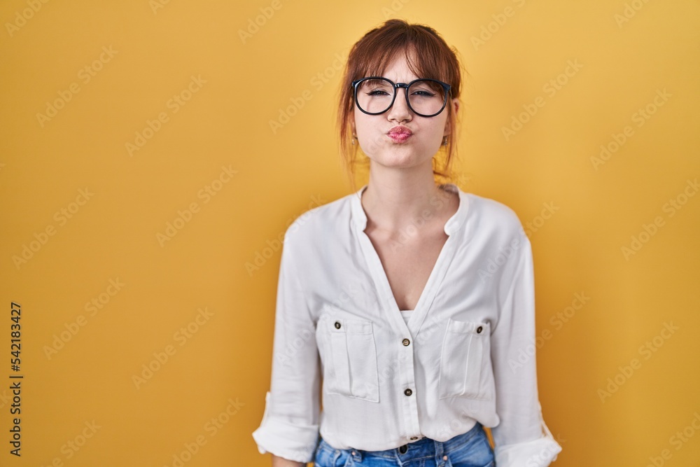 Young beautiful woman wearing casual shirt over yellow background puffing cheeks with funny face. mouth inflated with air, crazy expression.