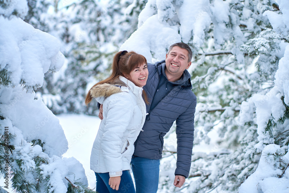 A joyful couple in love walking in winter forest heavy covered with snow