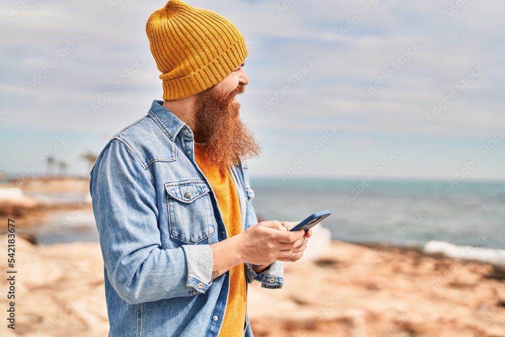 Young redhead man smiling confident using smartphone at seaside