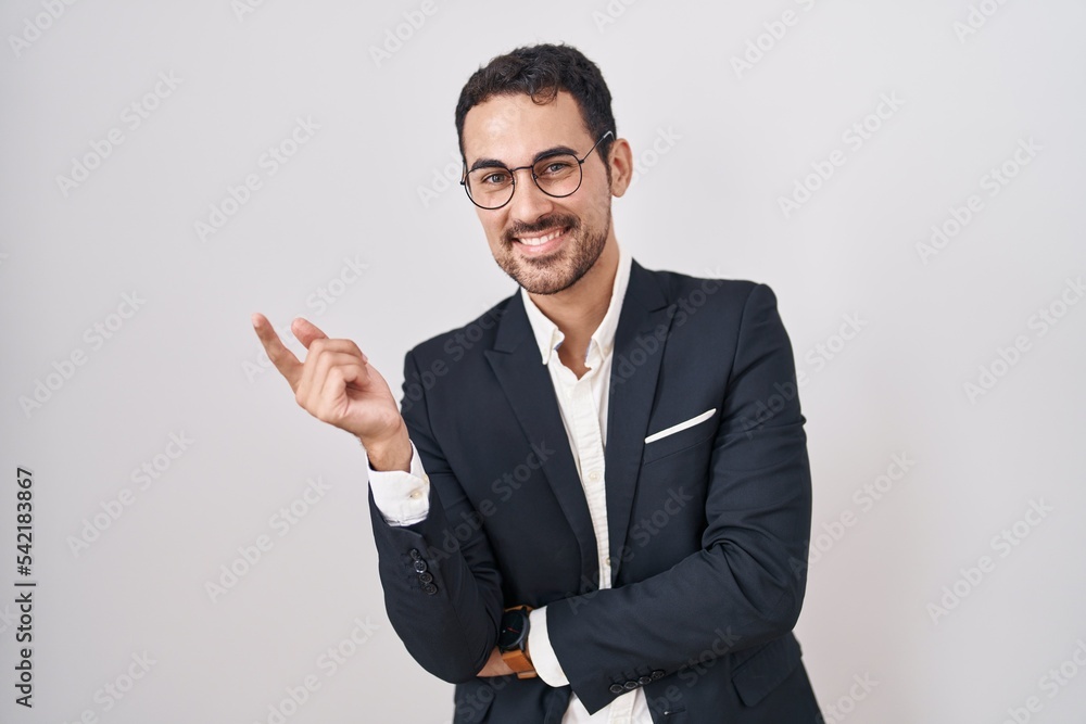 Handsome business hispanic man standing over white background with a big smile on face, pointing with hand finger to the side looking at the camera. Handsome business hispanic man standing over white background with a big smile on face, pointing with hand finger to the side looking at the camera.