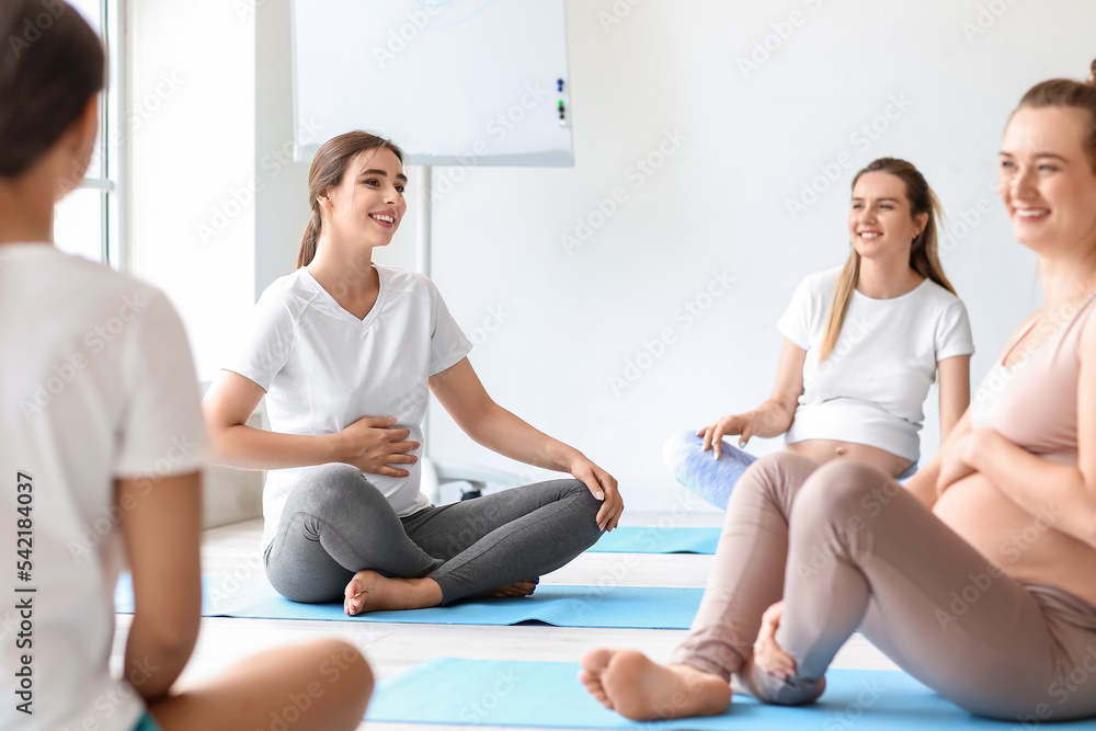 Young pregnant women doing yoga with coach in gym