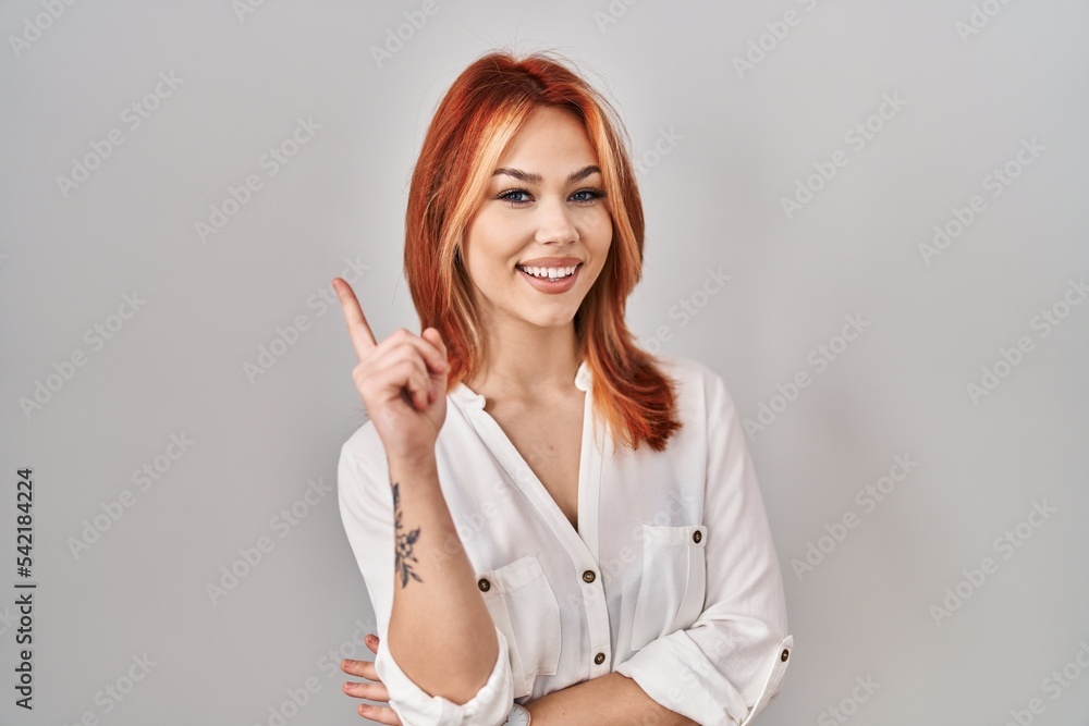 Young caucasian woman standing over isolated background with a big smile on face, pointing with hand finger to the side looking at the camera. Young caucasian woman standing over isolated background with a big smile on face, pointing with hand finger to the side looking at the camera.