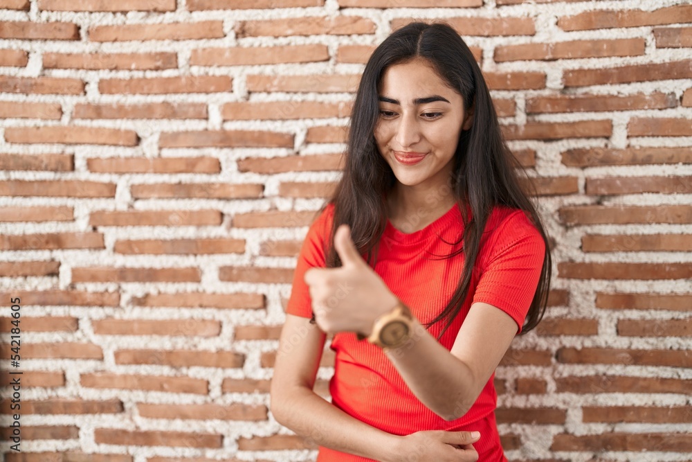 Young teenager girl standing over bricks wall looking proud, smiling doing thumbs up gesture to the side Young teenager girl standing over bricks wall looking proud, smiling doing thumbs up gesture to the side