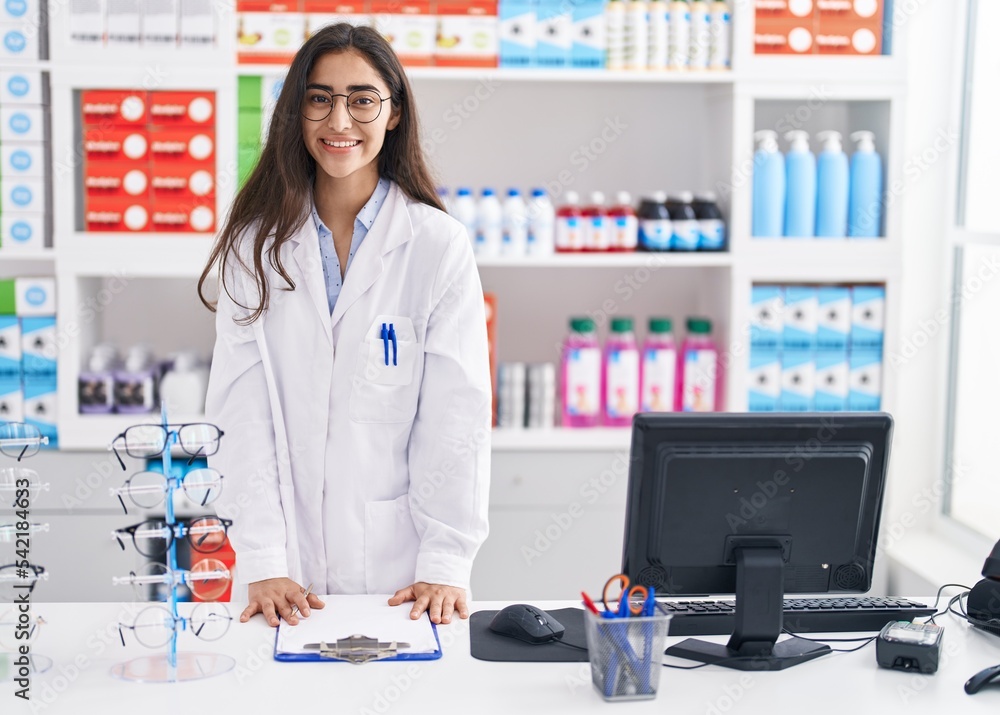 Young hispanic girl pharmacist writing on report clipboard at pharmacy Young hispanic girl pharmacist writing on report clipboard at pharmacy