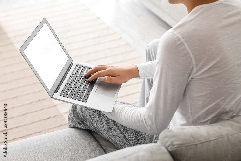 Young man using laptop on sofa at home, closeup Young man using laptop on sofa at home, closeup